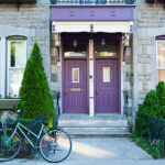 An old style house in the Plateau Mount Royal area in downtown Montreal with purple doors and trim and a bicycle parked in the front on the sidewalk.